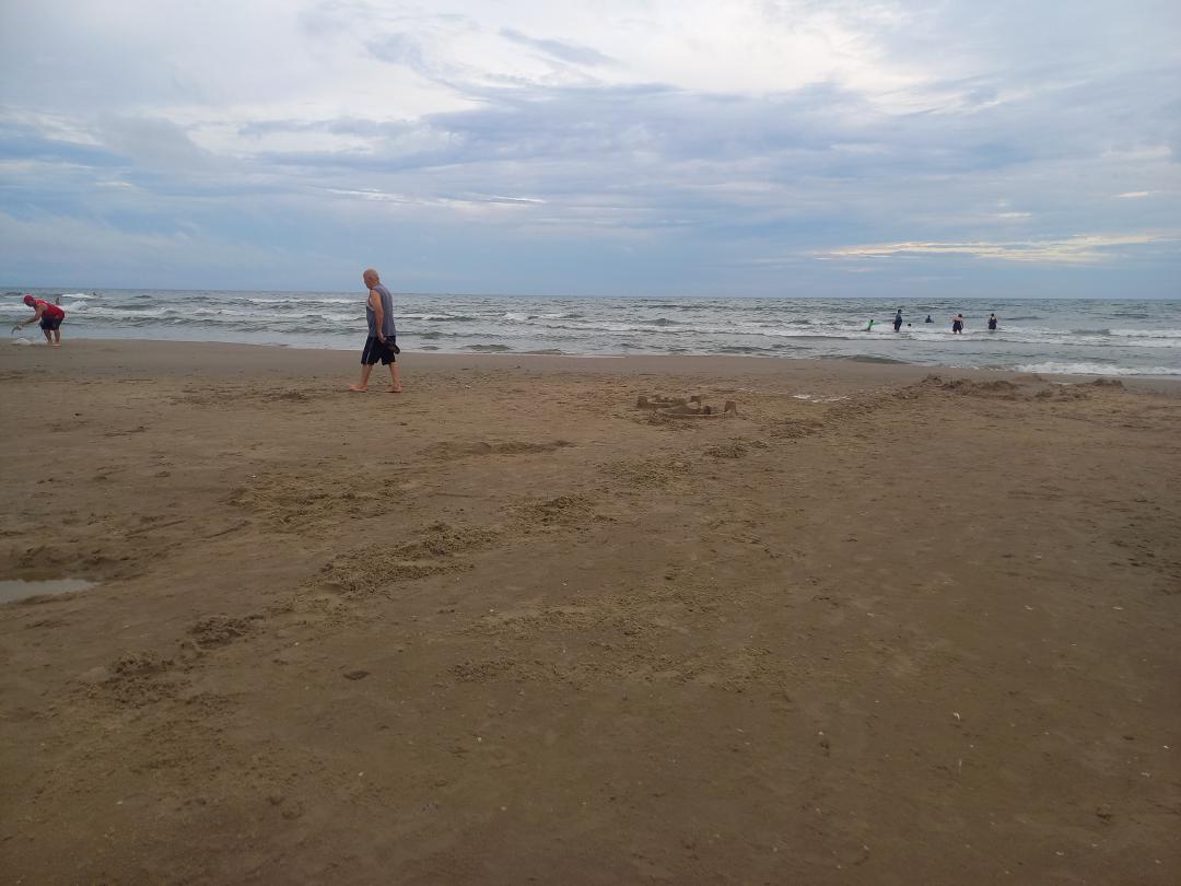 Beira da praia, com poucas pessoas, uma linha de areia remexida demarca o local onde antes haviam castelos de areia.