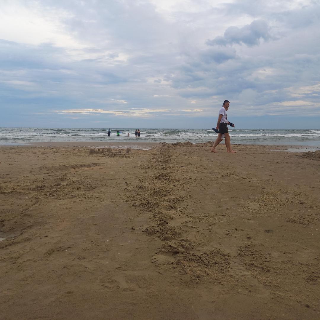 Beira da praia, com poucas pessoas, uma linha de areia remexida demarca o local onde antes haviam castelos de areia.