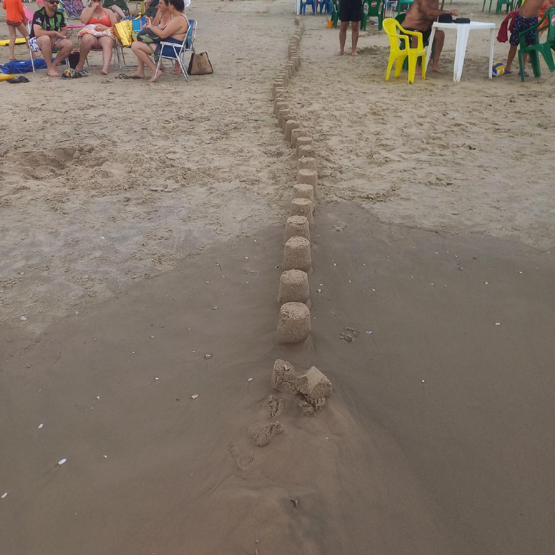 Uma linha contínua de castelos de areia parcialmente destruída pelas ondas do mar.