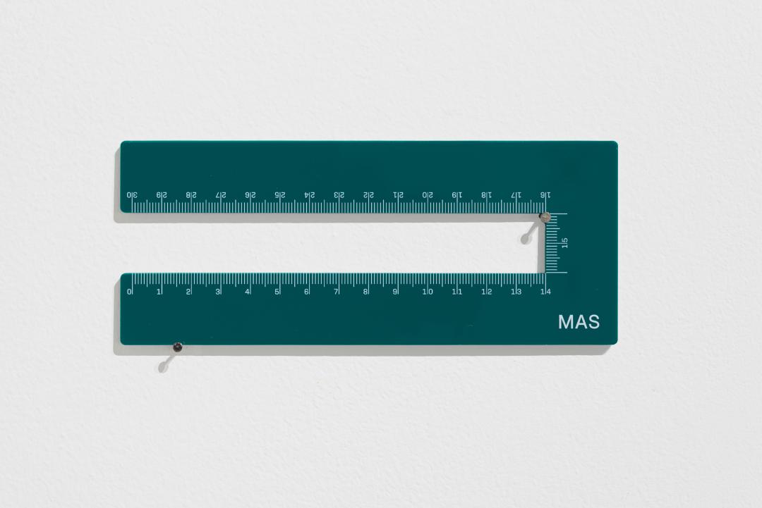 Uma régua verde de 30 centímetros distorcida. Nela está escrito: &ldquo;Mas&rdquo;.