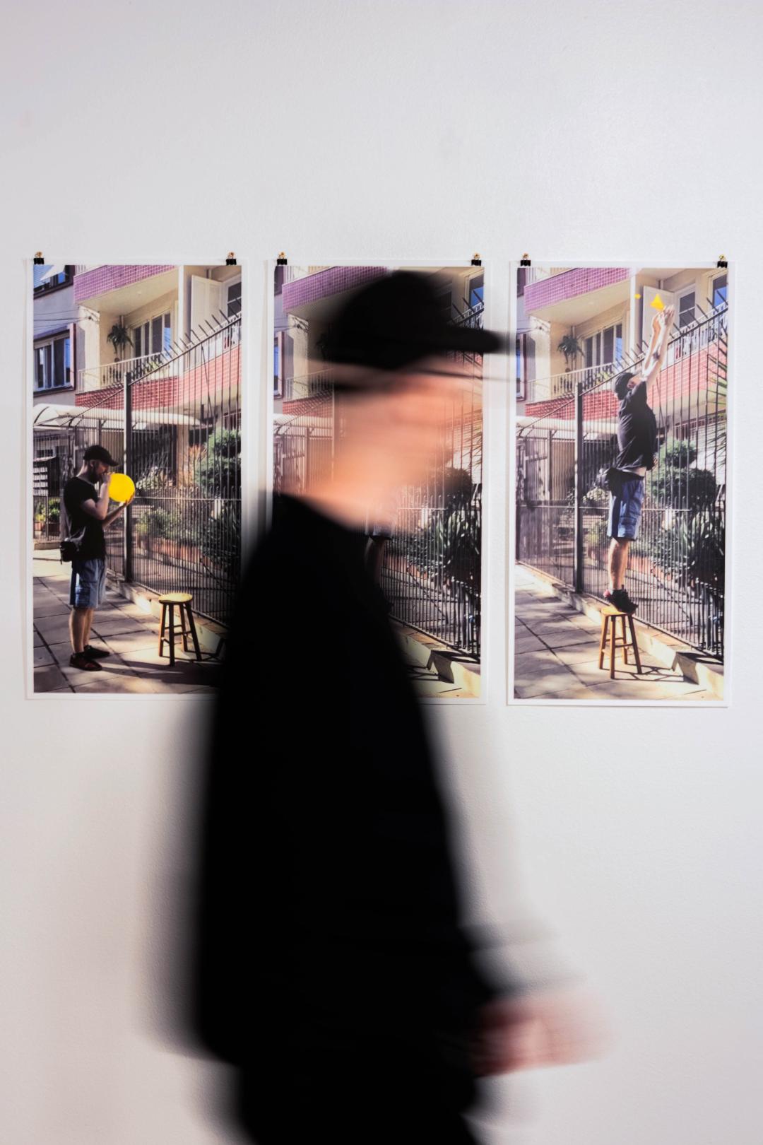 Uma pessoa com borrão de movimento passando em frente ao conjunto de fotos que compõem o trabalho.