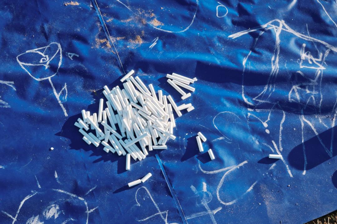 Close em uma parte de uma lona azul com vários desenhos feitos em giz branco.