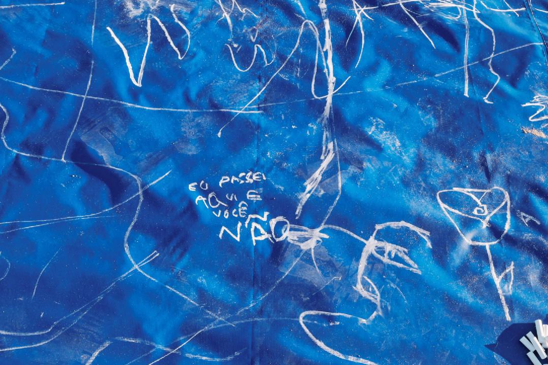 Close em uma parte de uma lona azul com vários desenhos feitos em giz branco.